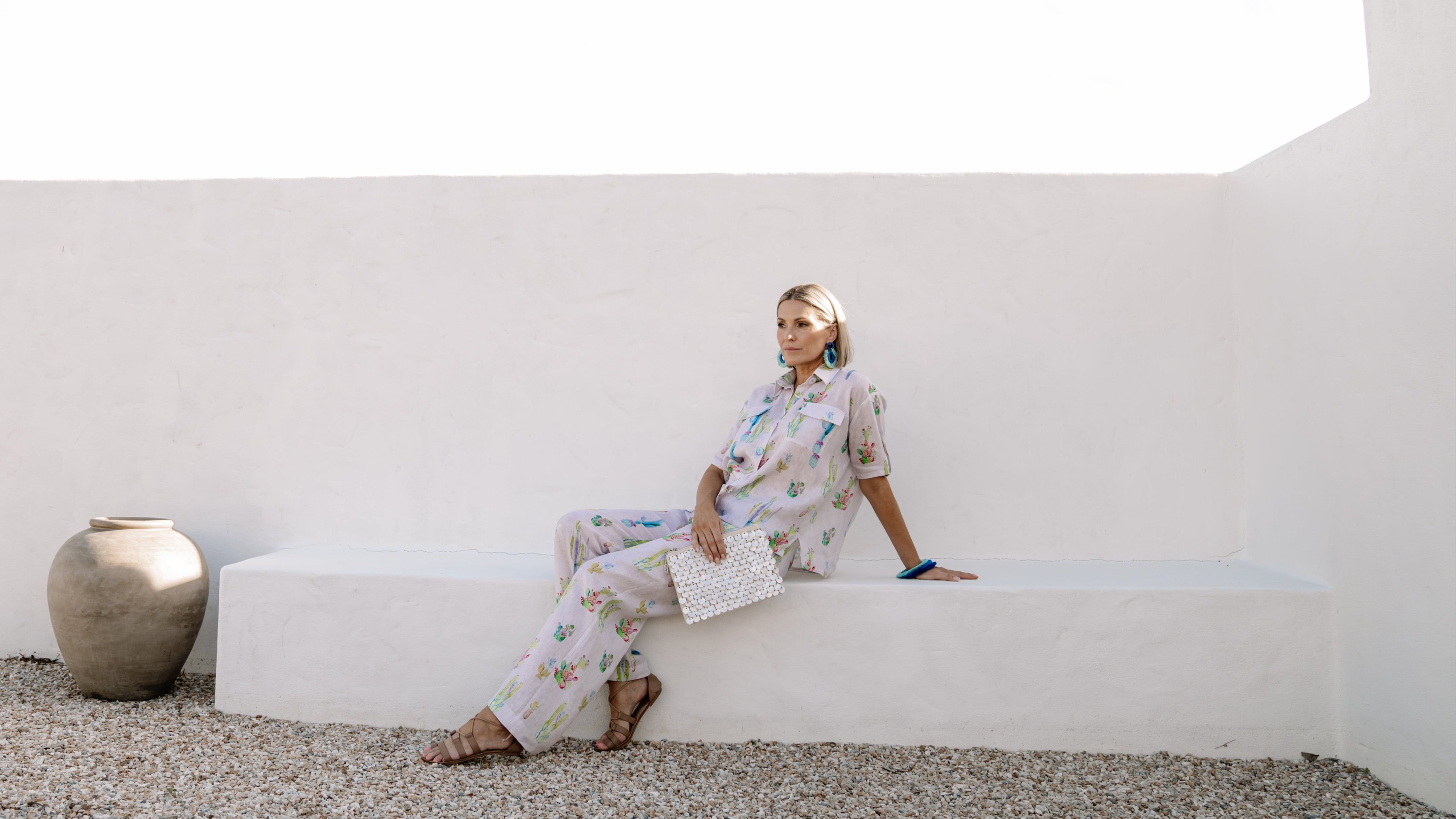 Woman sitting on a white bench in a minimalistic setting with a large vase.